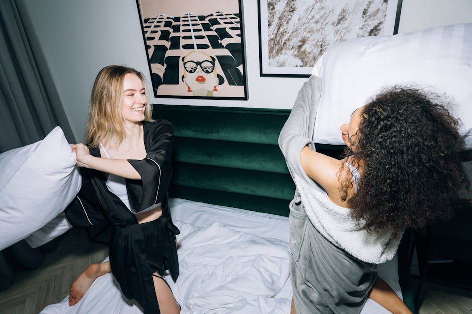 Two young women having a fun pillow fight in a cozy bedroom during a sleepover.