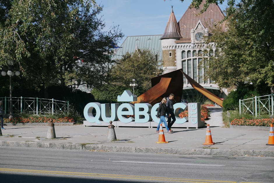 Tourists stroll by the famous Québec City sign in a sunny outdoor setting.