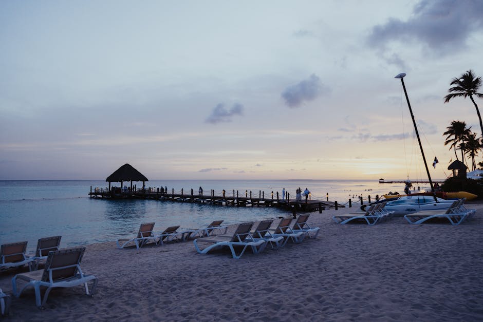 Relaxing beach scene with sunbeds and pier during sunset, perfect for travel inspiration.